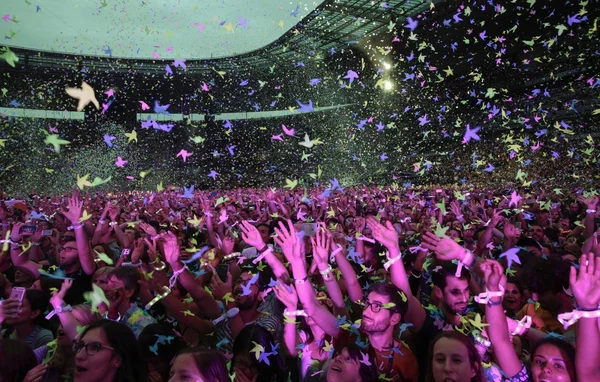 Spectateurs bras en l'air sous une pluie de confettis colorés et d'objets volants.