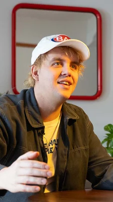 Un individu assis à une table portant une casquette avec un logo bleu et rouge.