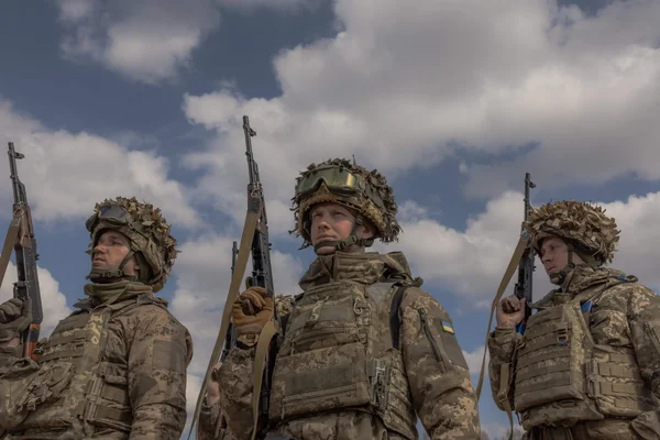 Trois soldats en tenue de combat armés de fusils se tenant en formation sous un ciel nuageux en Ukraine.