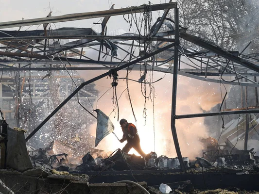 Un secouriste en gilet orange œuvrant dans les débris d'une structure effondrée et enfumée en Ukraine.