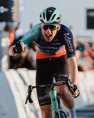 Paul Seixas leverait le poing en signe de victoire lors d'une course, revêtu de son équipement aux couleurs de Decathlon et Adecco.