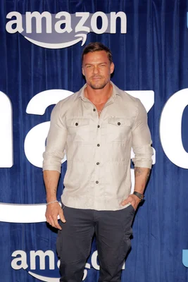 Alan Ritchson en chemise beige posant devant un fond bleu officiel Amazon.