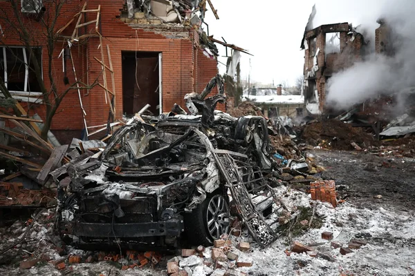 Une voiture détruites au milieu des ruines enneigées d'un quartier bombardé.