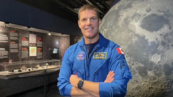 L'astronaute Jeremy Hansen en tenue bleue devant un modèle lunaire dans un musée