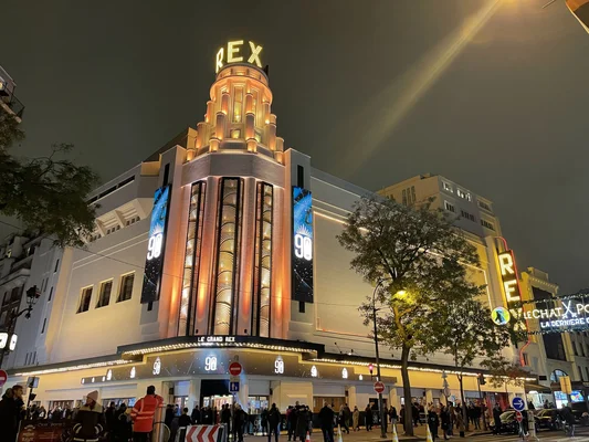 Le Grand Rex illuminé la nuit pour ses 90 ans, avec sa tour emblématique et une foule de piétons.