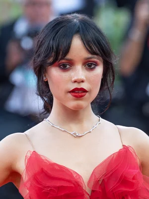 Jenna Ortega lors du 81ème Festival International du Film de Venise, arborant un maquillage rouge assorti à sa robe à volants.