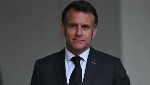 Emmanuel Macron en costume sombre devant un fond gris neutre.