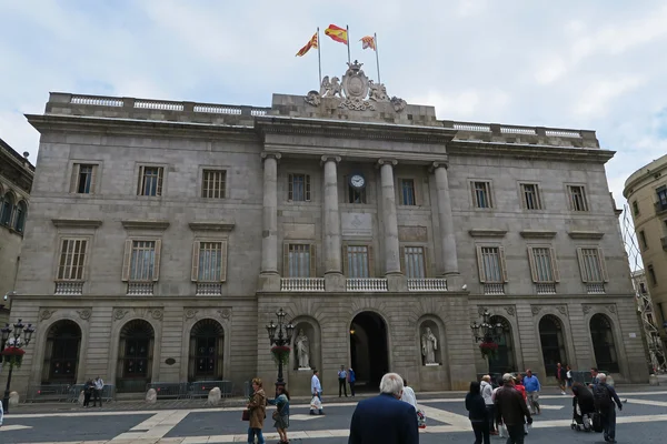 La Mairie de Barcelone, bâtiment historique en pierre avec colonnes et arcs, surplombant une place publique fréquentée par des passants.
