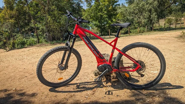 VTT électrique rouge et noir stationné sur un terrain accidenté.