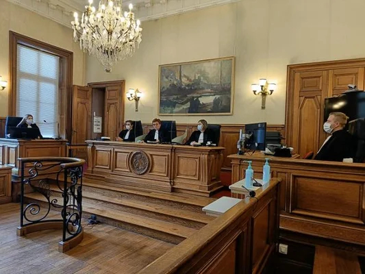 Vue d'une salle d'audience avec des lambris, un lustre et des magistrats en tenue officielle.