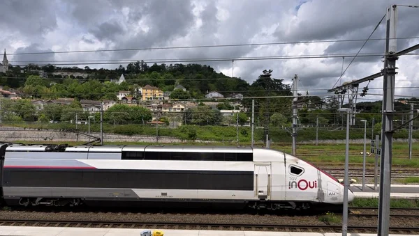 Un TGV InOui stationné sous un ciel nuageux avec un village en arrière-plan.