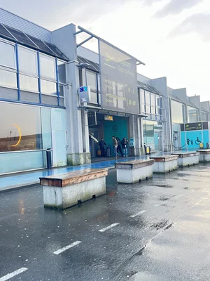 Accès départ de l'aéroport Nantes Atlantique avec sa façade vitrée et ses bancs en béton au premier plan.