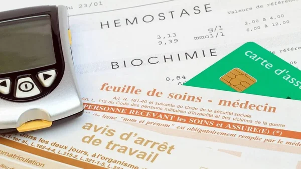 Un lecteur de glycémie, une feuille de soins et une carte Vitale posés sur une table.
