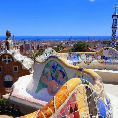 La façade ornée de l'Hôtel de Ville de Barcelone avec ses colonnes, arcs et drapeaux, sous un ciel bleu avec des personnes à sa base.