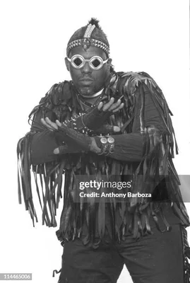 Afrika Bambaataa en tenue traditionnelle inspirée, mains croisées devant la poitrine.