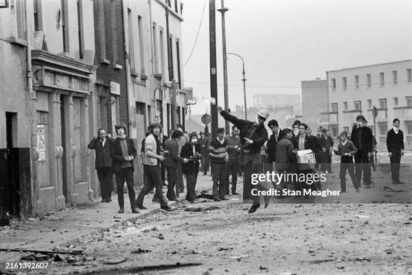 Émeute urbaine pendant le conflit nord-irlandais : un individu lançant un objet sur une rue couverte de débris