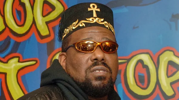 Afrika Bambaataa portant son casquette ankh distinctive devant un fond de graffiti.