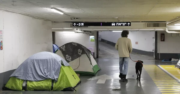 Un abri de fortune dans un parking souterrain avec des tentes et des habitants cherchant refuge.