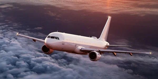 Un avion commercial blanc en vol au-dessus des nuages, sous un ciel sombre teinté des couleurs du coucher du soleil.