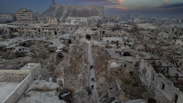 Dégâts urbains massifs avec une forteresse en fond de vue illustrant le coût de la reconstruction.