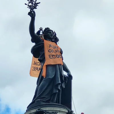 Statue ornée de bannières orange lors d'un rassemblement de soutien aux victimes de l'agent orange à Paris.