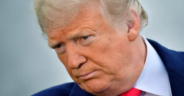 Gros plan sur Donald Trump en costume bleu et cravate rouge sur fond gris clair.