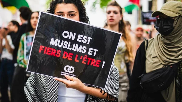 Manifestant levant un panneau 'ON EST MUSLIMS ET FIERS DE L'ÊTRE!' dans la foule.