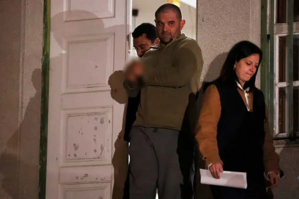 Trois personnes près d'une porte blanche écaillée et d'une fenêtre verte lors de l'interpellation nocturne au Portugal.