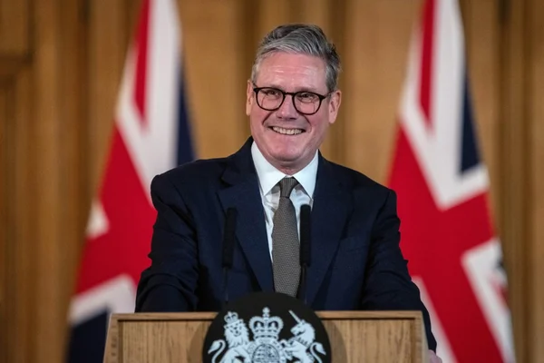 Keir Starmer s'adressant à la presse depuis un podium officiel britannique, devant deux drapeaux de l'Union Jack