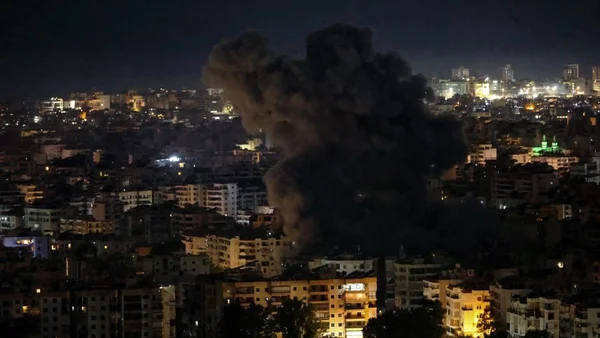 Vue nocturne de la banlieue sud de Beyrouth avec un panache de fumée noire après une frappe israélienne.