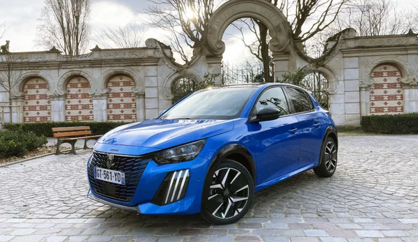 Une Peugeot 208 bleue garée devant une archère en pierre décorative dans un cadre urbain.