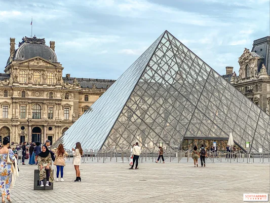 La pyramide d'entrée du Louvre avec le palais en arrière-plan et des visiteurs sur la cour pavée.