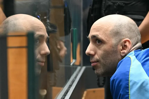 Cédric Jubillar, en veste bleue, se penche vers une vitre dans un environnement formel.
