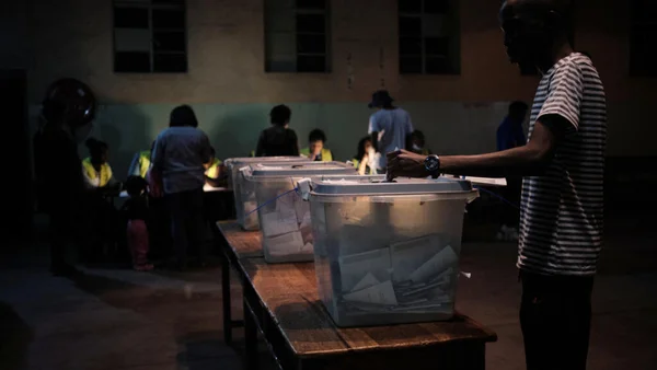 Un électeur zimbabwéen déposant son bulletin dans l'urne lors d'un scrutin dans une salle faiblement éclairée.