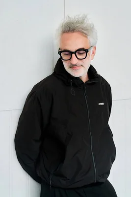 Vincent Delerm debout, mains dans les poches, devant un mur clair.