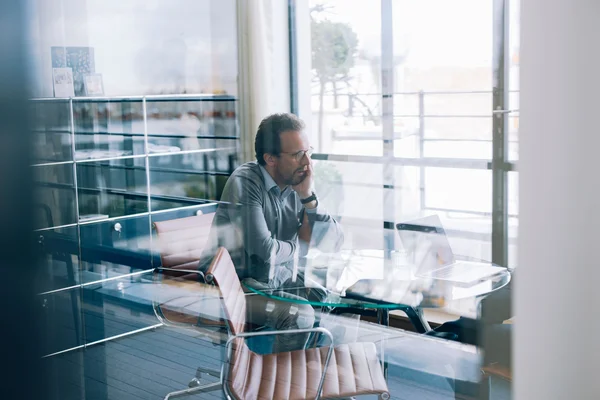 François Durvye en pull gris, pensif devant son ordinateur portable dans un bureau moderne lumineux.
