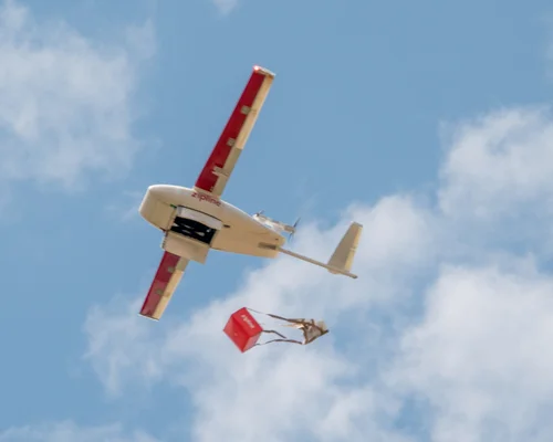 Un drone Zipline larguant un colis sous parachute lors d'une livraison aérienne.