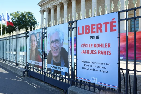 Affiches de soutien à Cécile Kohler et Jacques Paris sur une grille devant un bâtiment officiel aux couleurs françaises.