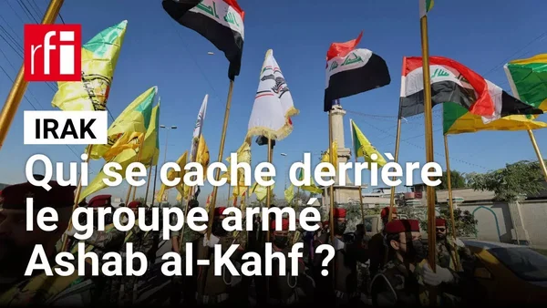 Des hommes en tenue militaire brandissant des drapeaux irakiens et des drapeaux verts et jaunes d'Ashab al-Kahf.