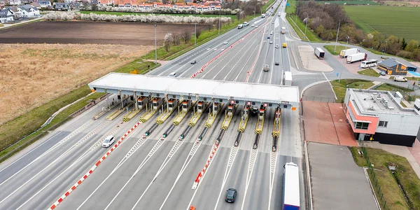 Vue aérienne d'un péage autoroutier avec cabines jaunes et noires sous toit blanc, au milieu des champs.