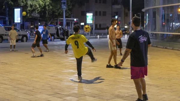 Des habitants jouent au football dans une place urbaine de Tel-Aviv pendant la nuit.