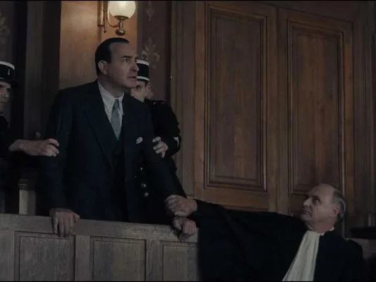 Scène de tribunal du film avec un homme en costume maintenu par des officiers et un magistrat en robe.
