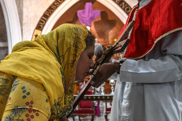 Une femme voilée embrassant un crucifix devant une personne en aube à l'intérieur d'une église.