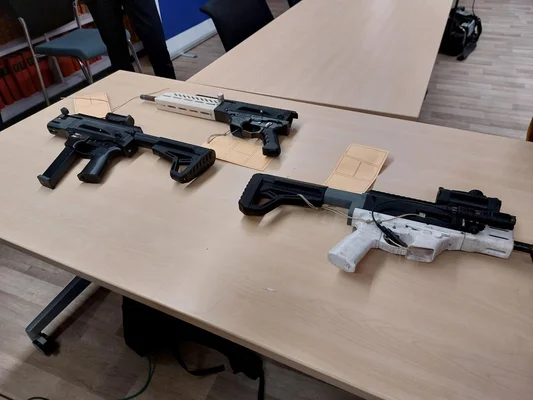 Trois armes à feu, deux noires et une blanche, disposées sur une table en bois clair dans un intérieur domestique.