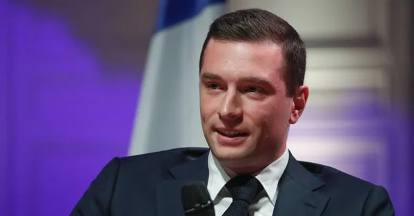 Un homme en costume parlant au micro devant un fond éclairé en violet.