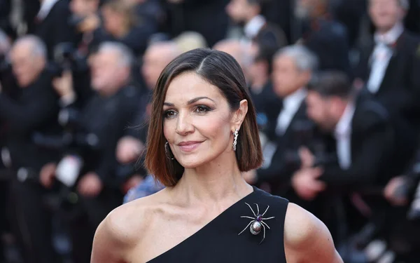 Nadia Farès en robe noire asymétrique avec une broche araignée lors d'une soirée.