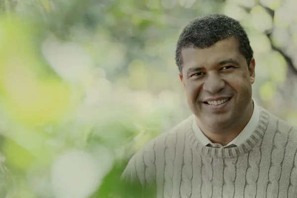 Adam Oyebanji souriant dans un cadre extérieur verdoyant.