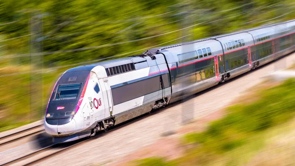 Un TGV InOui avec sa livrée blanche, argent et rose roulant sur les voies.