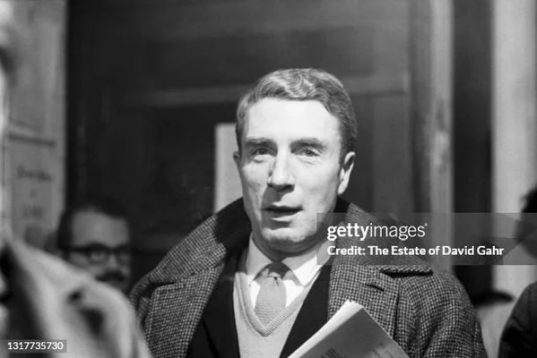 Portrait photographique d'un homme portant une veste tweed et tenant un document.