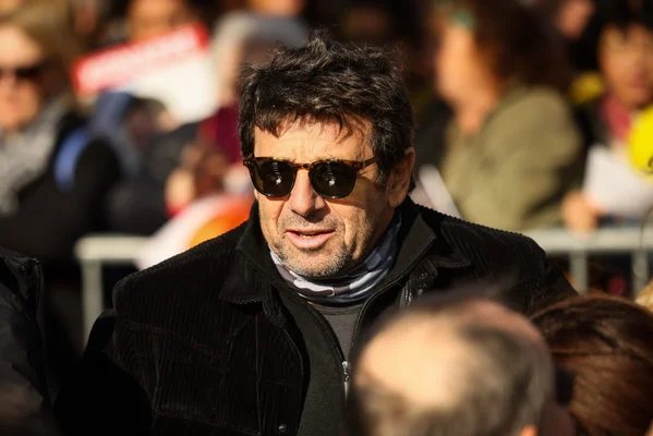 Patrick Bruel portant des lunettes de soleil et une écharpe grise.